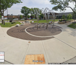Screenshot 2026-07-15 084407 - OccuPaws Circular brick plaza with a looping metal arch sculpture, surrounding benches and trees in a campus-style courtyard.